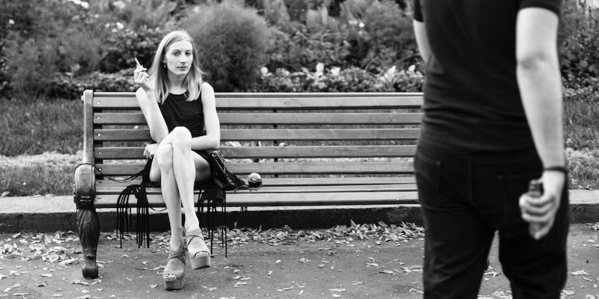 Girl smoking on a park bench while boyfriend walks away.