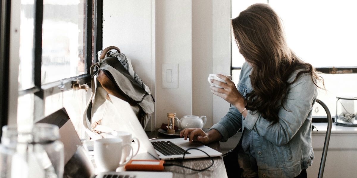A man holding a white teacup while typing on a laptop.