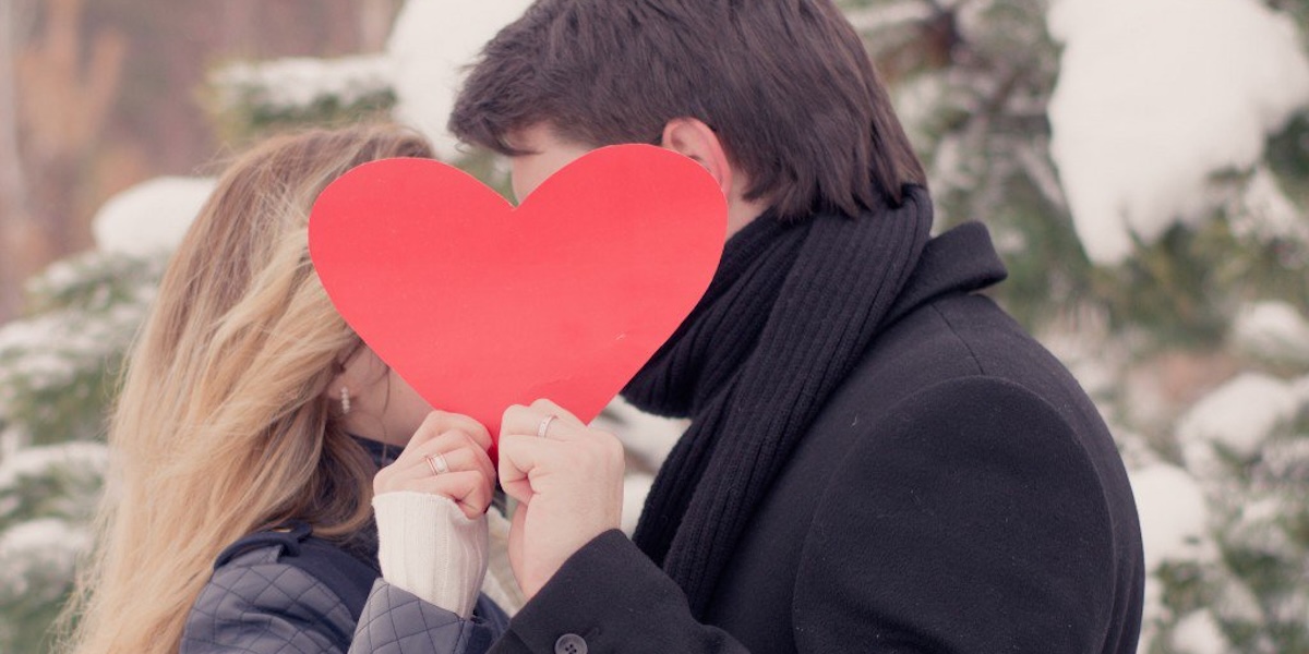 Lovers kissing while holding a red heart