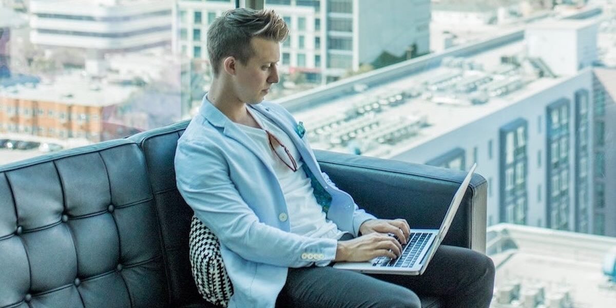 Writer sitting on couch typing on laptop.